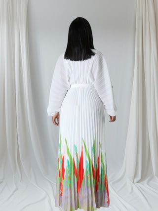 Person wearing a white top and colorful pleated skirt against a white curtain background