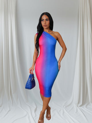 Model posing in pink and blue ombré one-shoulder dress styled with clear heels and handbag for chic evening look.