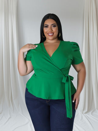 Woman wearing an emerald green puff sleeve wrap blouse with tie waist — flattering peplum-style top for curvy women from Tulley’s Boutique.