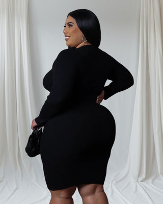 Model wearing Fine & Fluffy Sweater Dress in black with belted waist detail, holding small handbag.