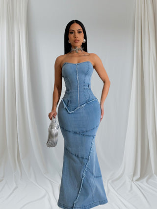 Woman wearing strapless denim corset maxi dress with structured bodice and fitted silhouette, accessorized with silver jewelry and clutch.