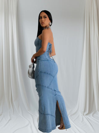 Woman wearing strapless denim corset maxi dress with structured bodice and fitted silhouette, accessorized with silver jewelry and clutch.