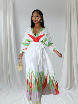 Woman wearing a flowy white pleated maxi dress with multicolor floral brushstroke design and tie waist — Vibrant Garden Harmony Dress from Tulley’s Boutique.
