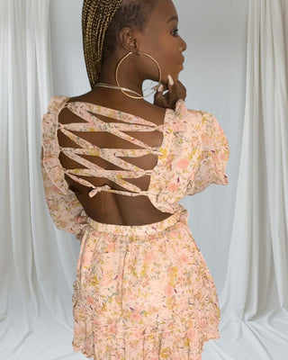 Woman wearing a floral print mini dress with ruffled hem and lace-up open back — feminine summer style from Tulley’s Boutique.