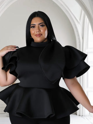 Plus-size model wearing a black mock neck peplum top with dramatic ruffle sleeves and a fitted waist.