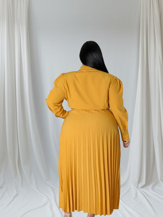 Person wearing a mustard yellow dress against a white curtain background