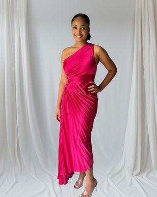 Woman wearing one-shoulder blush pink pleated maxi dress with flowing skirt — elegant evening gown from Tulley’s Boutique.