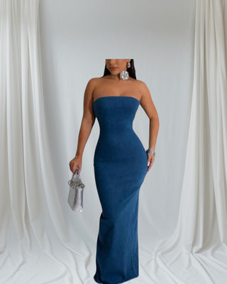 Woman wearing strapless blue denim maxi dress with fitted silhouette, back slit, and silver accessories — Tulley’s Boutique.