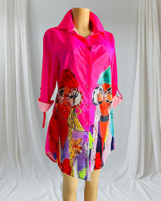 Woman wearing a hot pink button-up shirt dress with bold illustrated faces and rolled sleeves — vibrant art-inspired fashion from Tulley’s Boutique.