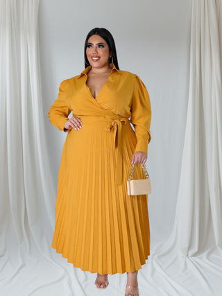 Woman wearing a caramel long-sleeve wrap pleated maxi dress — elegant plus-size fashion piece from Tulley’s Boutique.