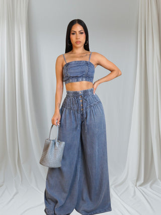 Woman wearing a denim outfit with wide-leg pants and a crop top against a white curtain background.