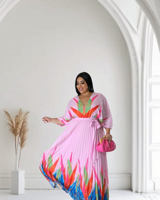 Model in a pink pleated maxi dress with colorful leaf patterns, featuring a V-neck and flowing sleeves, exuding elegance
