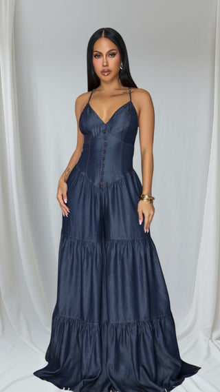 Navy blue satin jumpsuit with v-neckline, spaghetti straps and tiered wide-leg design. Elegant silhouette against white backdrop.