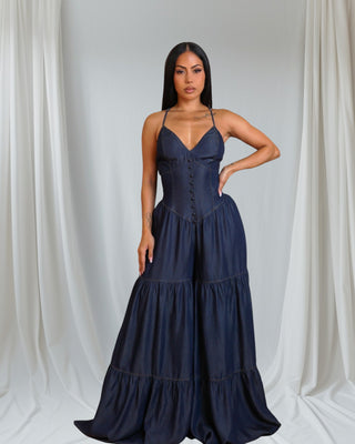 Navy blue satin jumpsuit with v-neckline, spaghetti straps and tiered wide-leg design. Elegant silhouette against white backdrop.