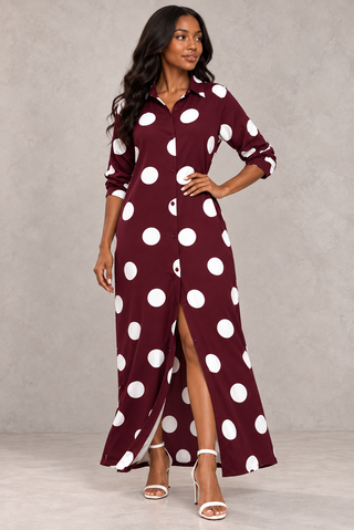 Model in a burgundy polka dot button-down maxi dress with one hand on her hip and the long sleeves rolled up