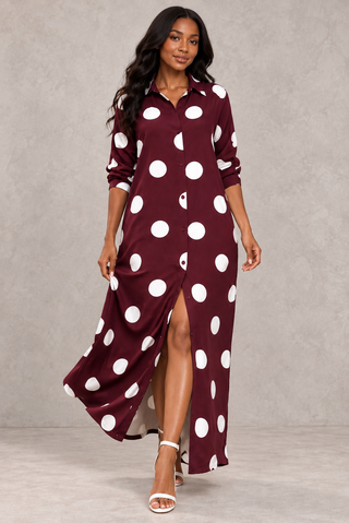 Model walking in a burgundy maxi shirt dress with white polka dots, the front slit open as the skirt moves, worn with white strappy heels