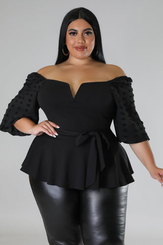 Woman wearing a black off-shoulder peplum top with ruffled sleeves on a gray background
