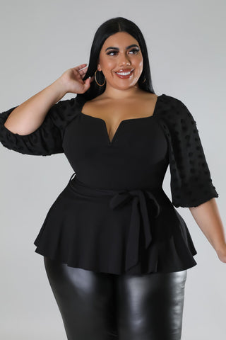 Woman wearing a black peplum top with a plain background