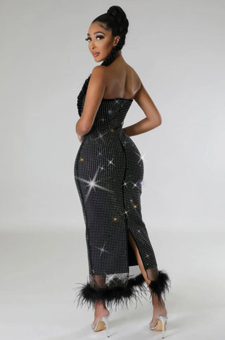 Woman wearing a black strapless jumpsuit with star patterns and feather details on a white background
