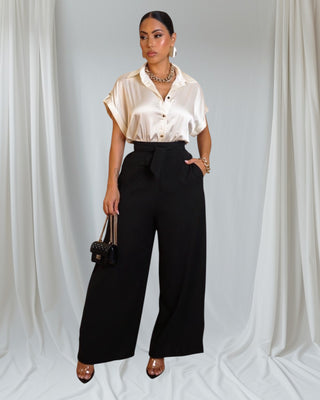 Woman wearing a beige blouse and black pants against a plain background
