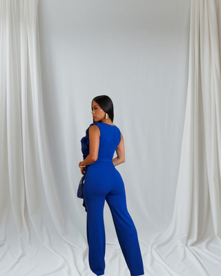 Woman in vibrant royal blue jumpsuit with elegant ruffled neckline and wide-leg silhouette, sleeveless and waist tie included