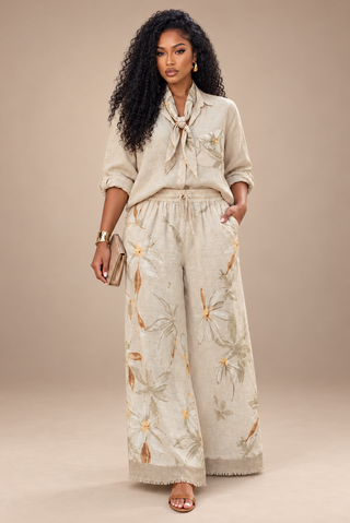 Model wearing a cream floral linen pants set with a button-front shirt, neck-tied scarf and wide-leg pants with a fringe hem