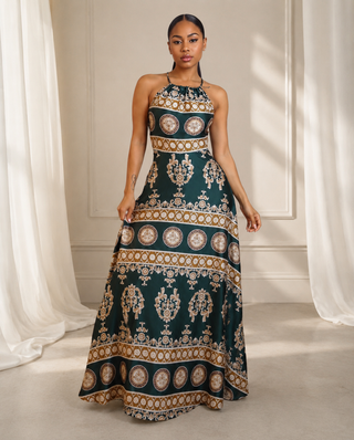 A woman modeling a sleeveless halter-neck maxi dress with a dark teal green base and ornate gold and beige baroque-style patterns.