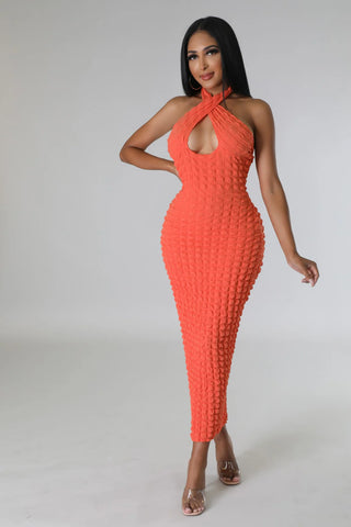 Woman wearing a coral halter bubble fabric maxi dress with low back and stretch fit.