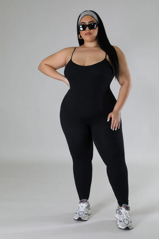 Woman wearing a black stretch sleeveless jumpsuit with U neckline and adjustable straps.