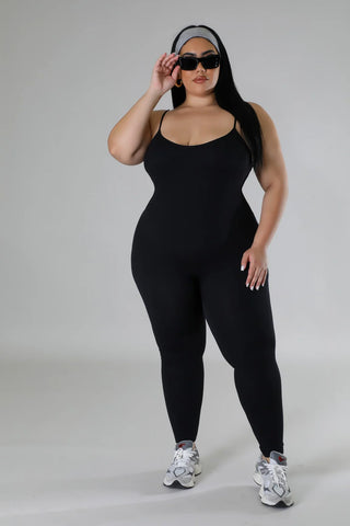 Woman wearing a black stretch sleeveless jumpsuit with U neckline and adjustable straps.