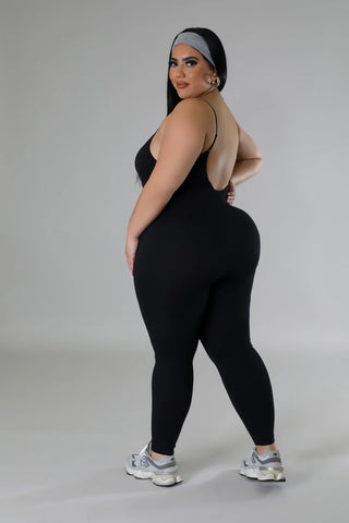 Woman wearing a black stretch sleeveless jumpsuit with U neckline and adjustable straps.