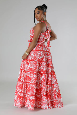 A woman modeling a red and white floral tiered maxi dress with a halter-style back and side cutouts, photographed against a light gray studio background.
