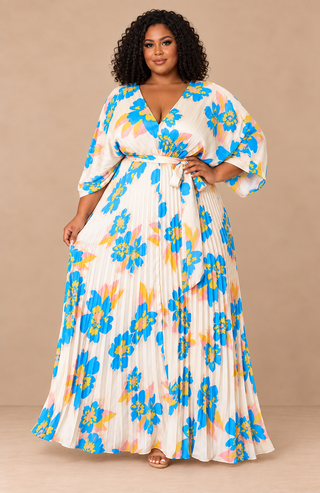 Plus-size model wearing an ivory floral pleated maxi dress with blue, yellow, and blush flowers, V-neckline, and self-tie waist