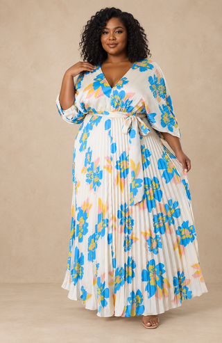Plus-size model wearing an ivory floral pleated maxi dress with blue, yellow, and blush flowers, V-neckline, and self-tie waist