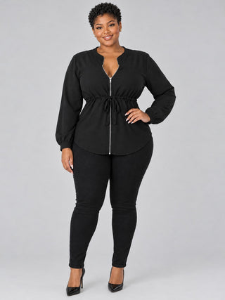 Plus size model wearing a black zip-front tie-waist blouse zipped to the split neckline with black skinny jeans and heels
