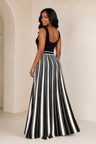     Model wearing the Bold Direction black sleeveless maxi dress with a cream striped full skirt and self-tie waist, front view.