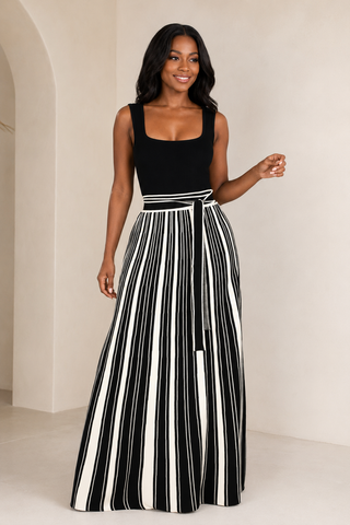     Model wearing the Bold Direction black sleeveless maxi dress with a cream striped full skirt and self-tie waist, front view.