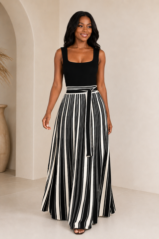     Model wearing the Bold Direction black sleeveless maxi dress with a cream striped full skirt and self-tie waist, front view.
