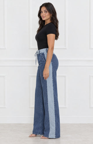 Side profile of wide-leg denim stripe drawstring pants showing the full-length light-wash side stripe and relaxed wide leg