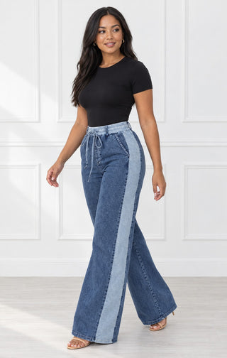 Three-quarter view of high-waisted wide-leg denim pants with light-wash side stripe and tie drawstring waist, styled with a black bodysuit and nude heels