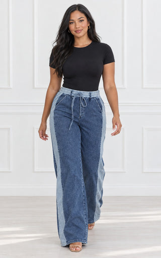 Model walking in high-waisted wide-leg denim stripe drawstring pants showing the movement of the wide legs, styled with a black bodysuit