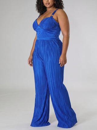 Three-quarter side view of a plus size model in the Elegant royal blue satin wide-leg jumpsuit, showing the pleated bodice, adjustable straps, defined waist and flowing pleated wide legs