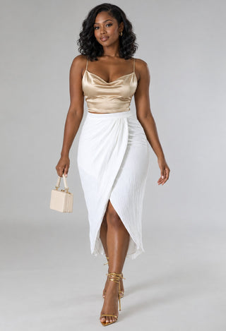 Model walking in an ivory wrap midi skirt as the front slit opens, paired with a champagne satin cami and cream handbag