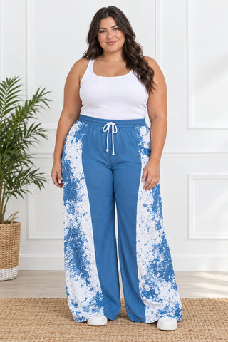 Plus size model in blue and white paint-splash wide-leg pants with solid blue front panel and drawstring waist, styled with white tank and sneakers