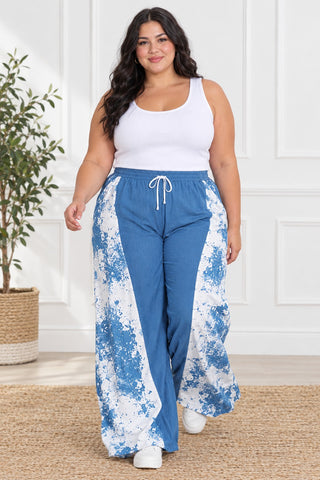 Plus size model walking in flowing blue and white paint-splash wide-leg drawstring pants