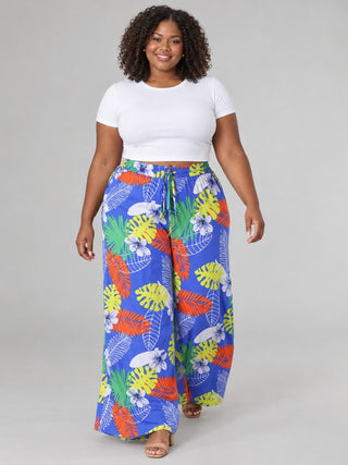 Plus size model walking in royal blue tropical print wide-leg pants with drawstring waist, white crop tee and tan sandals