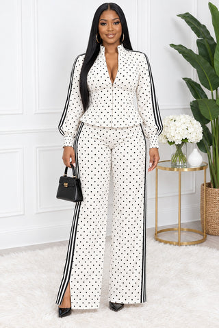 Model wearing the Polka Perfect ivory polka dot set, front view: zip-front stand-collar peplum top with black striped sleeves and matching striped wide-leg pants