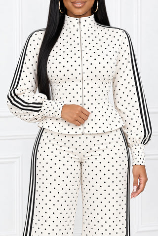 Close-up of the ivory polka dot peplum top: stand collar, front zipper, fitted waist, black sleeve stripes and smocked cuff