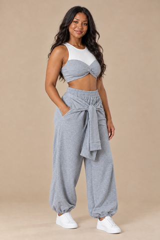 Three-quarter view of the heather gray crop top and jogger pants set showing the knotted tie sleeves at the waist and gathered ankle cuffs, styled with white sneakers