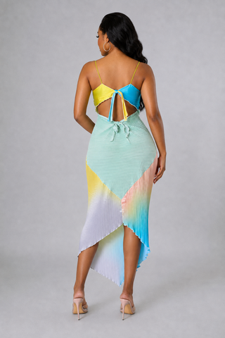 Back view Model wearing the Sunset Sorbet multicolor pleated asymmetrical midi dress with spaghetti straps and a pastel rainbow design
